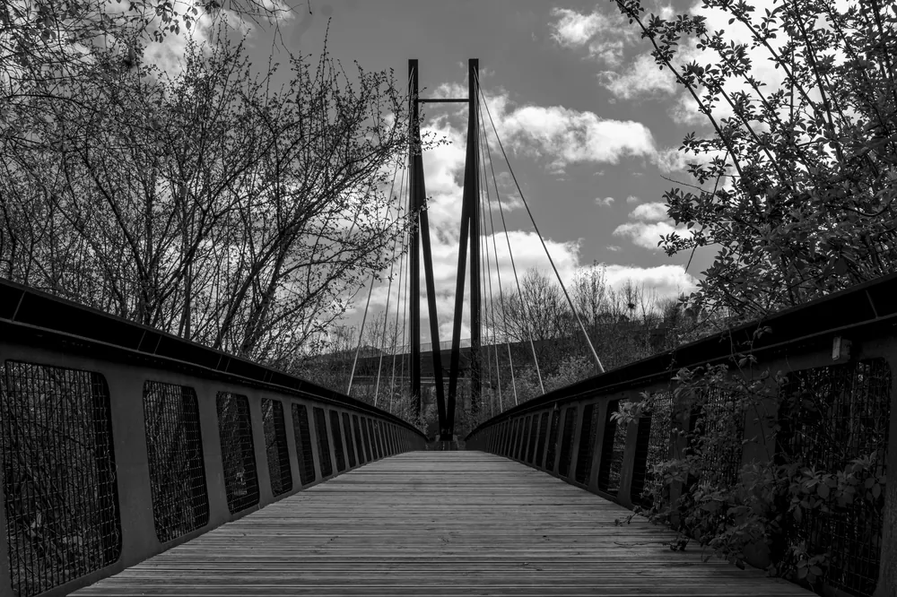 Pasarela atirantada de madera, en blanco y negro, con el pilono al fondo